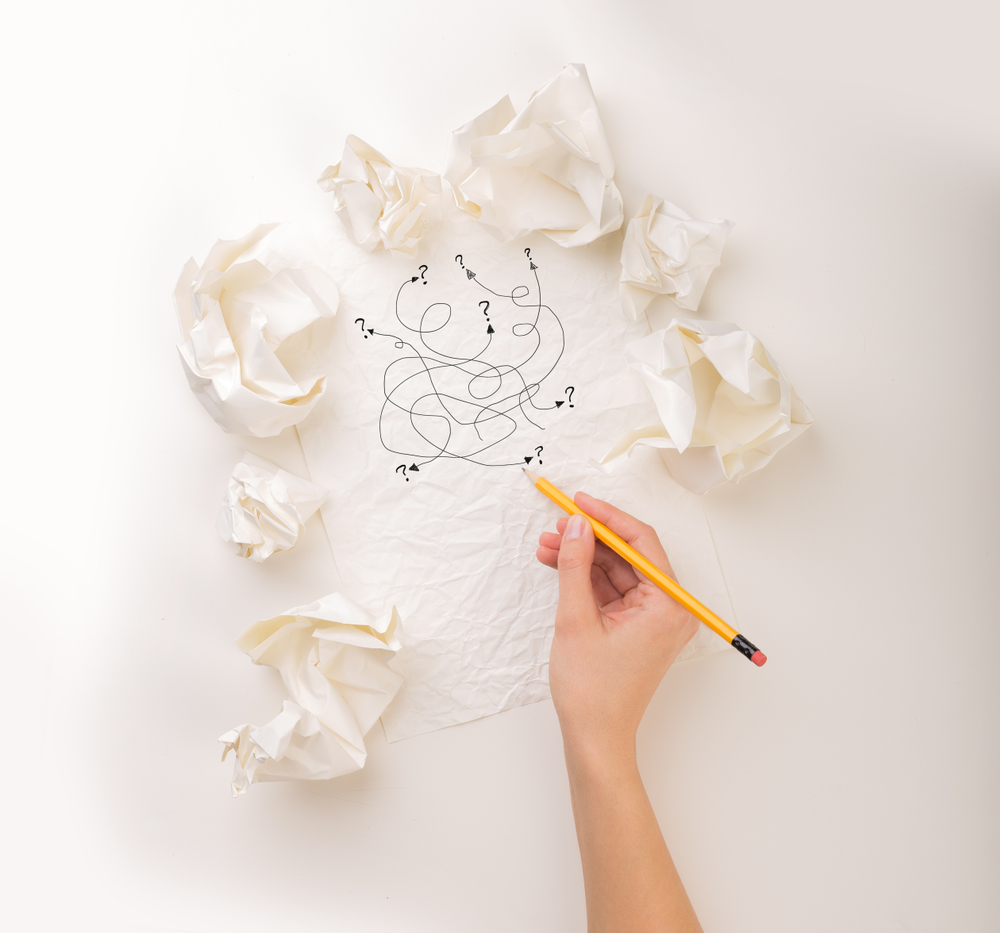 Female hand next to a few crumpled paper balls drawing random scribbles